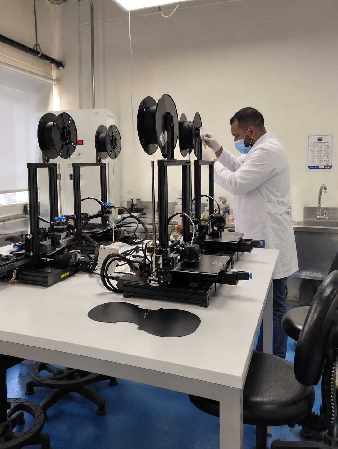 Technician in a lab coat loading filament into a row of 3D printers in a lab