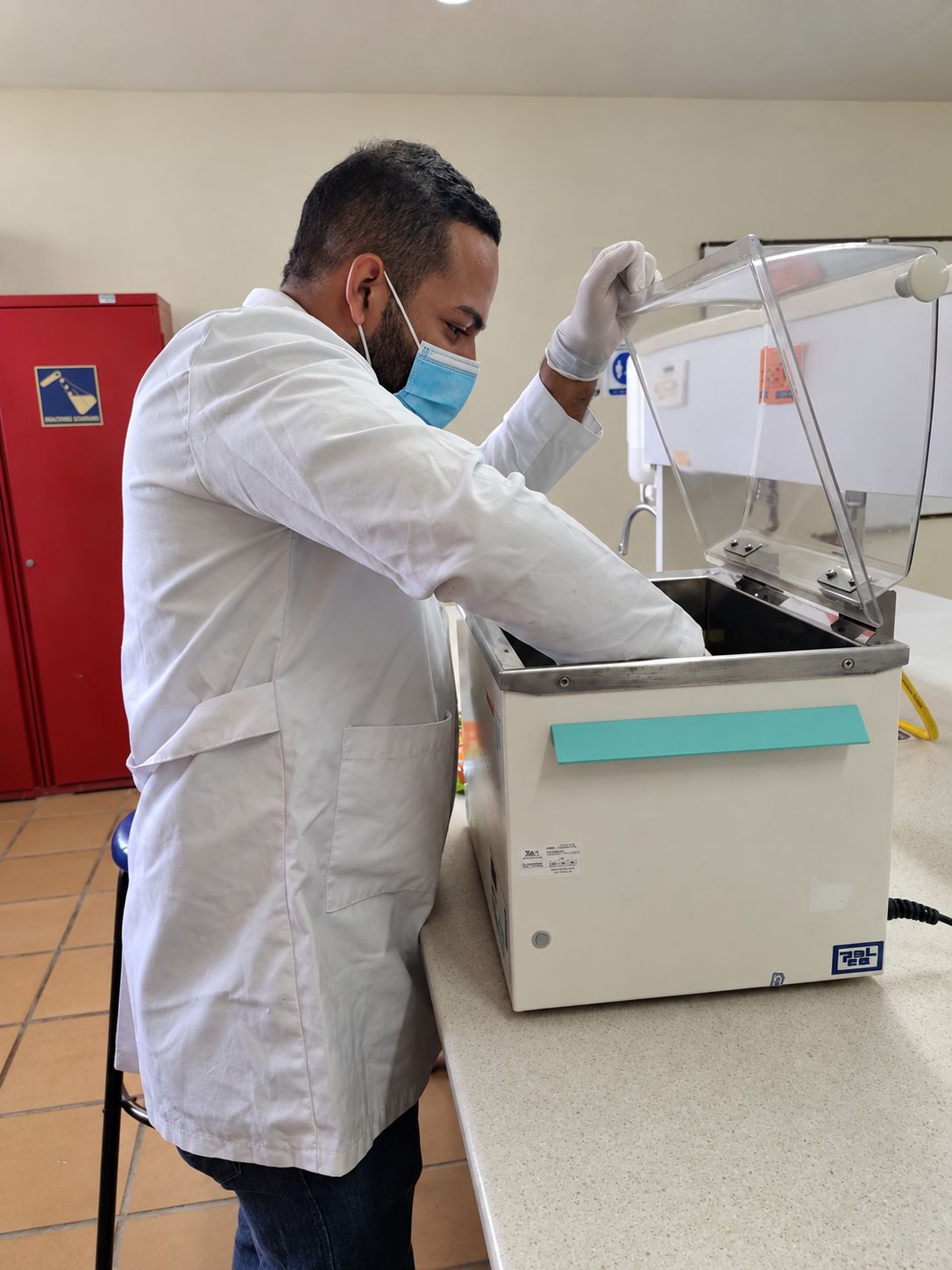 Technician in a lab coat and gloves checking the inside of a laboratory water bath